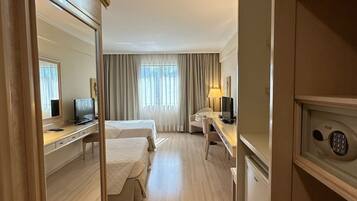 Quarto de hotel com cama, escrivaninha, cadeira, televisão e cofre.