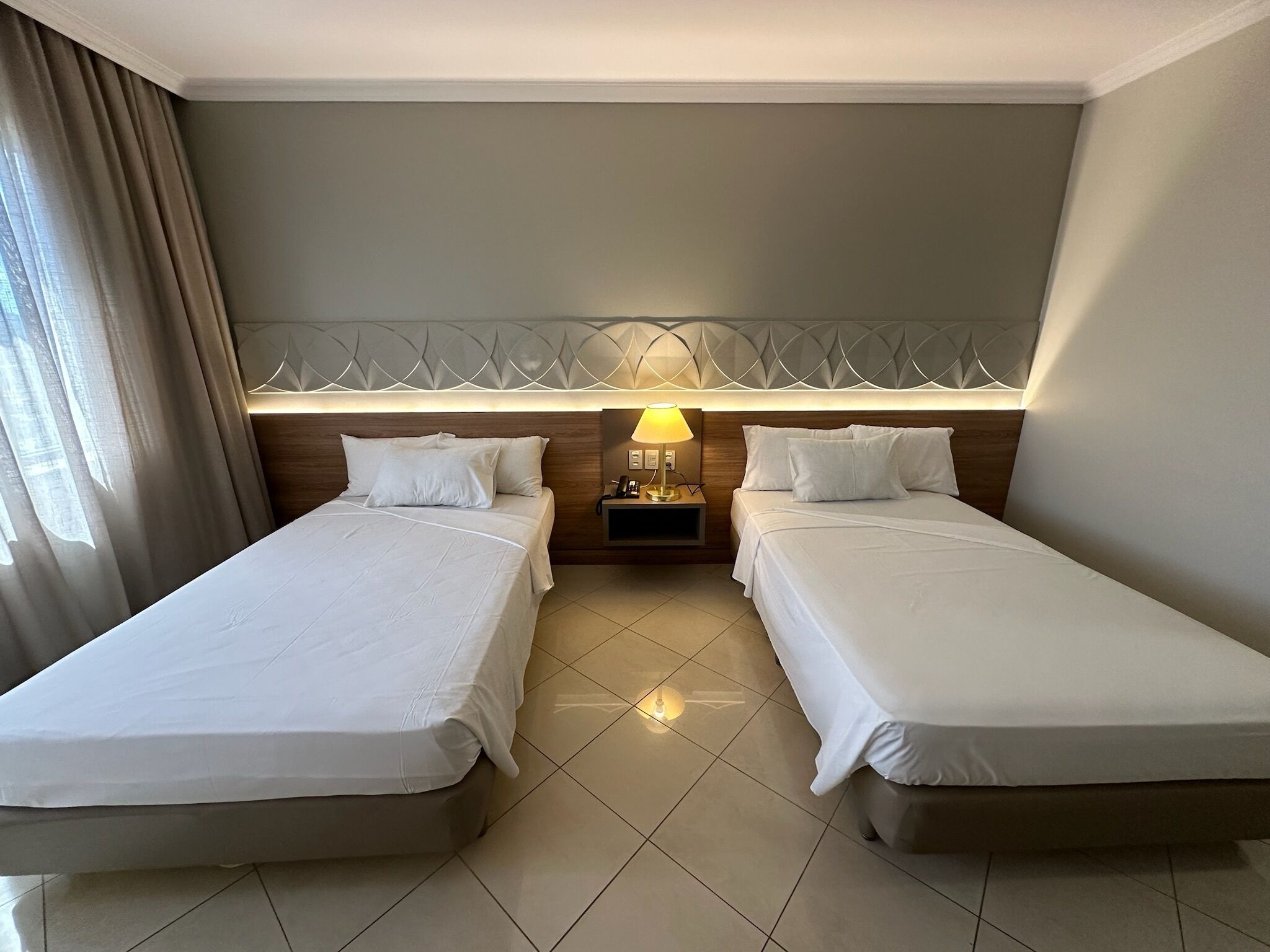 Une chambre d’hôtel avec deux lits simples, une table de chevet avec une lampe et une tête de lit décorative.