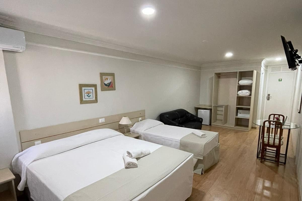 A hotel room with two beds, a desk, a chair, and a TV.