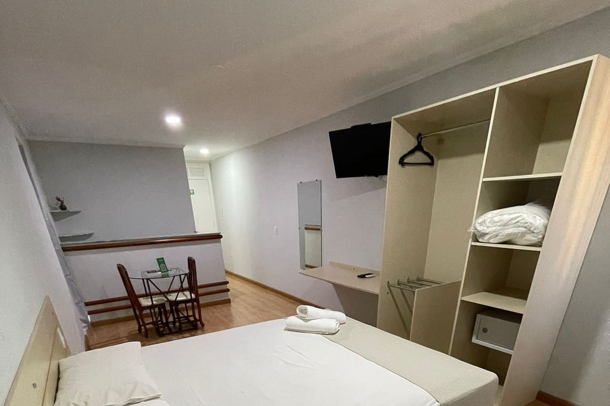 A bedroom with a bed, a chair, a desk, a mirror, and a wardrobe.