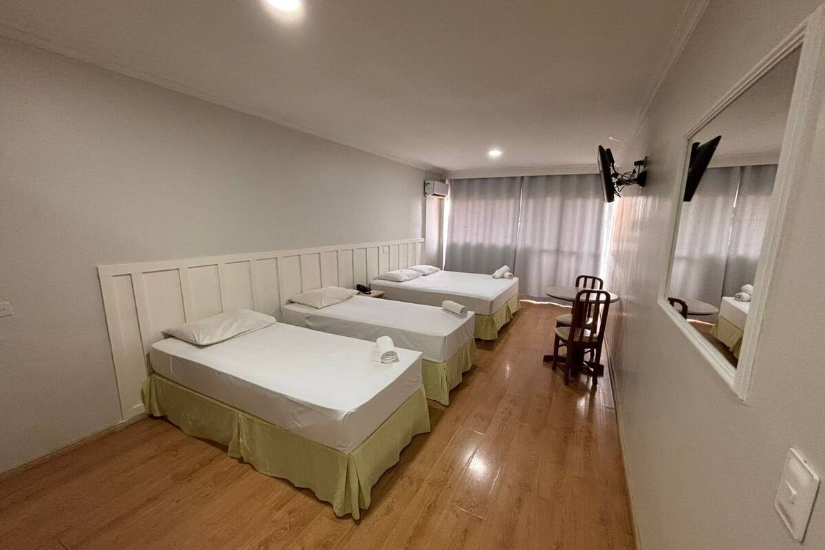A hotel room with three single beds, a small table, a chair, and a mirror on the wall.