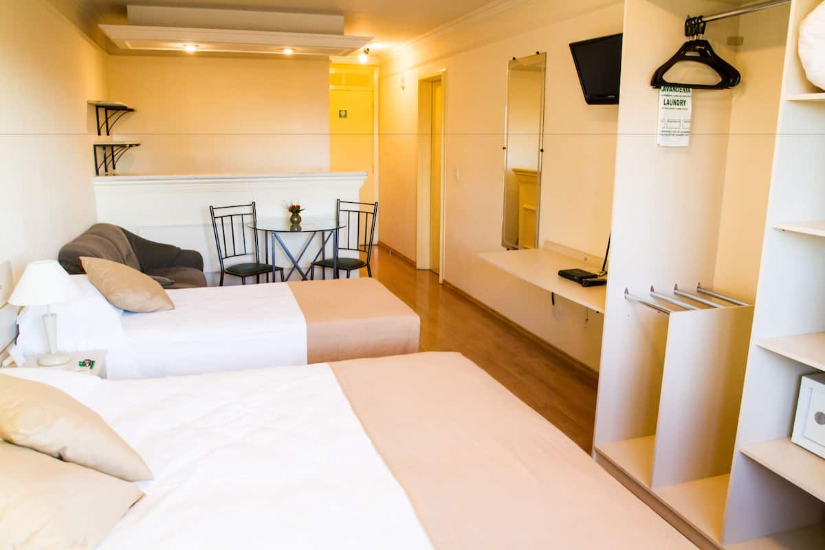 A hotel room with two beds, a small table with chairs, a mirror, a TV, and a sign indicating a laundry area.