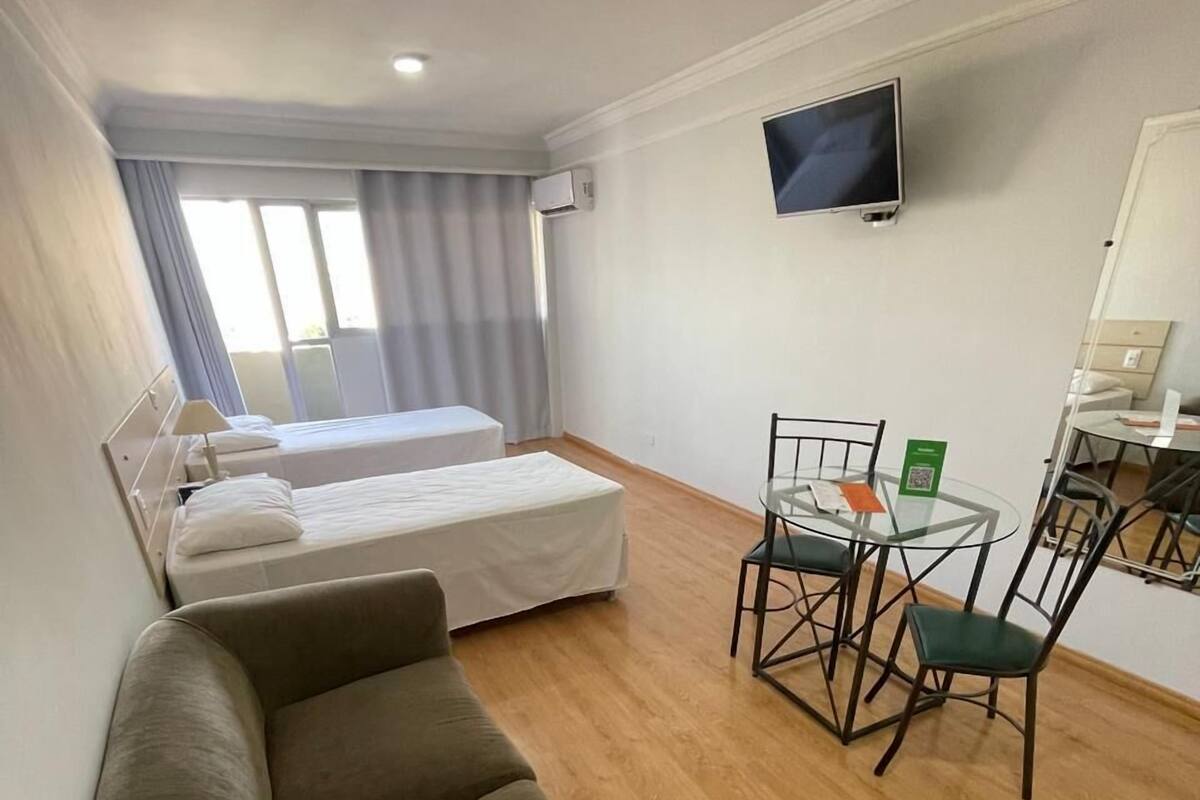 A room with a sofa, two beds, a TV, and a dining area with chairs and a table.