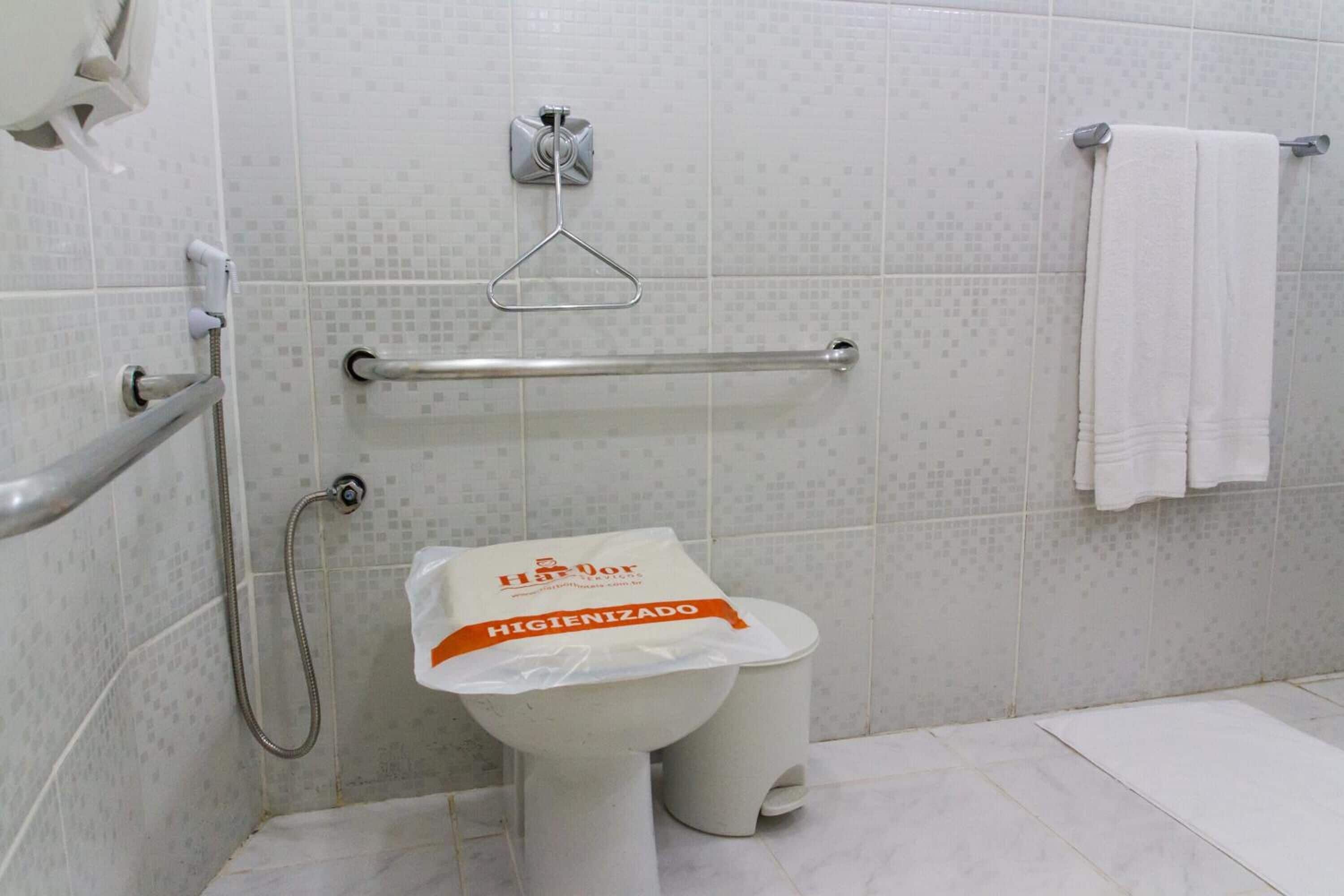 Baño con inodoro, barras de apoyo, ducha y perchero para toallas.