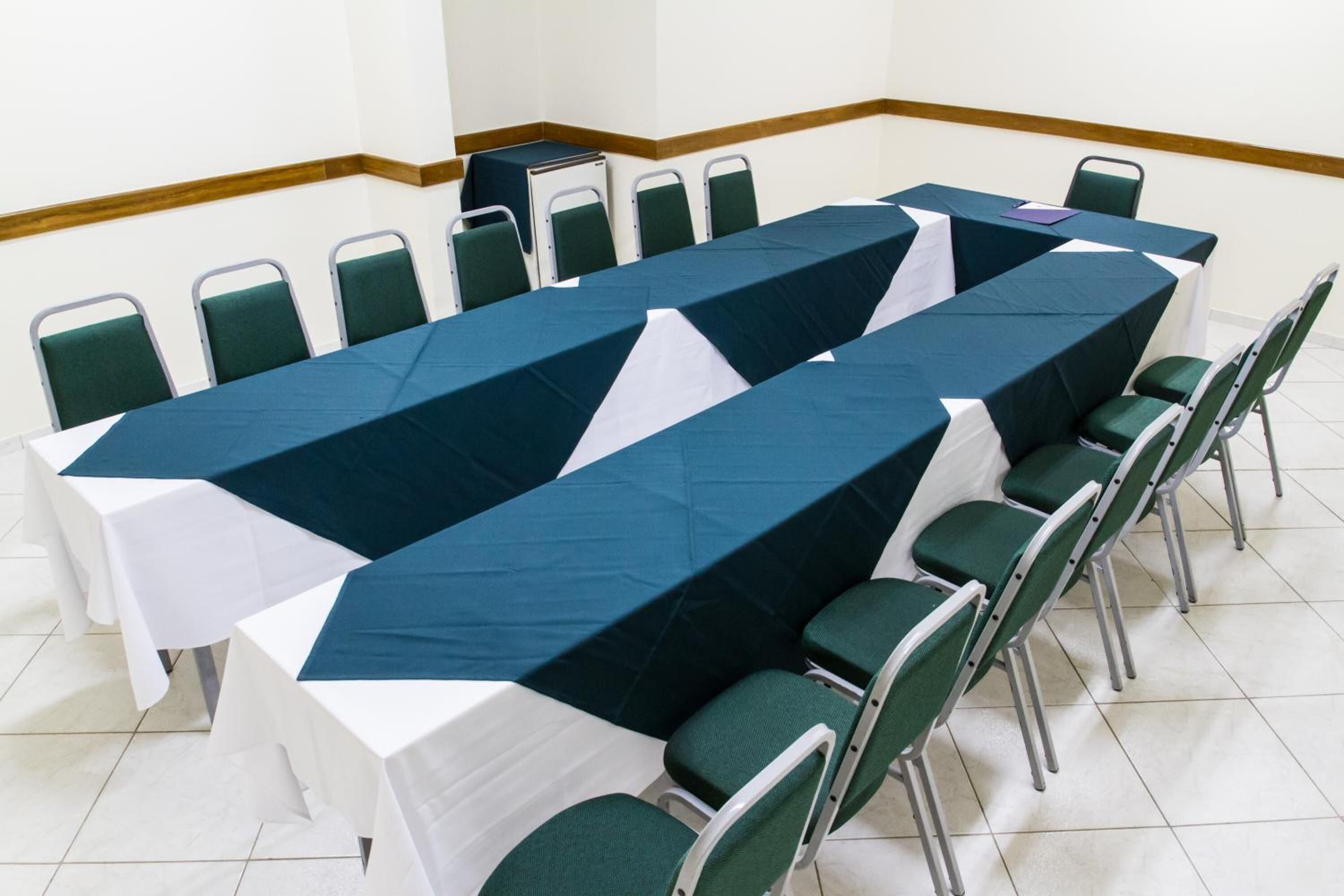 Une salle de conférence avec une longue table recouverte d’une nappe bleue et blanche, entourée de chaises vertes.