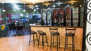 Uma área de bar com piso ladrilhado, banquetas de metal preto e um balcão com armários de vidro exibindo garrafas.