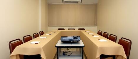 A conference room with a long table, chairs, an air conditioning unit, and a projector on a table.
