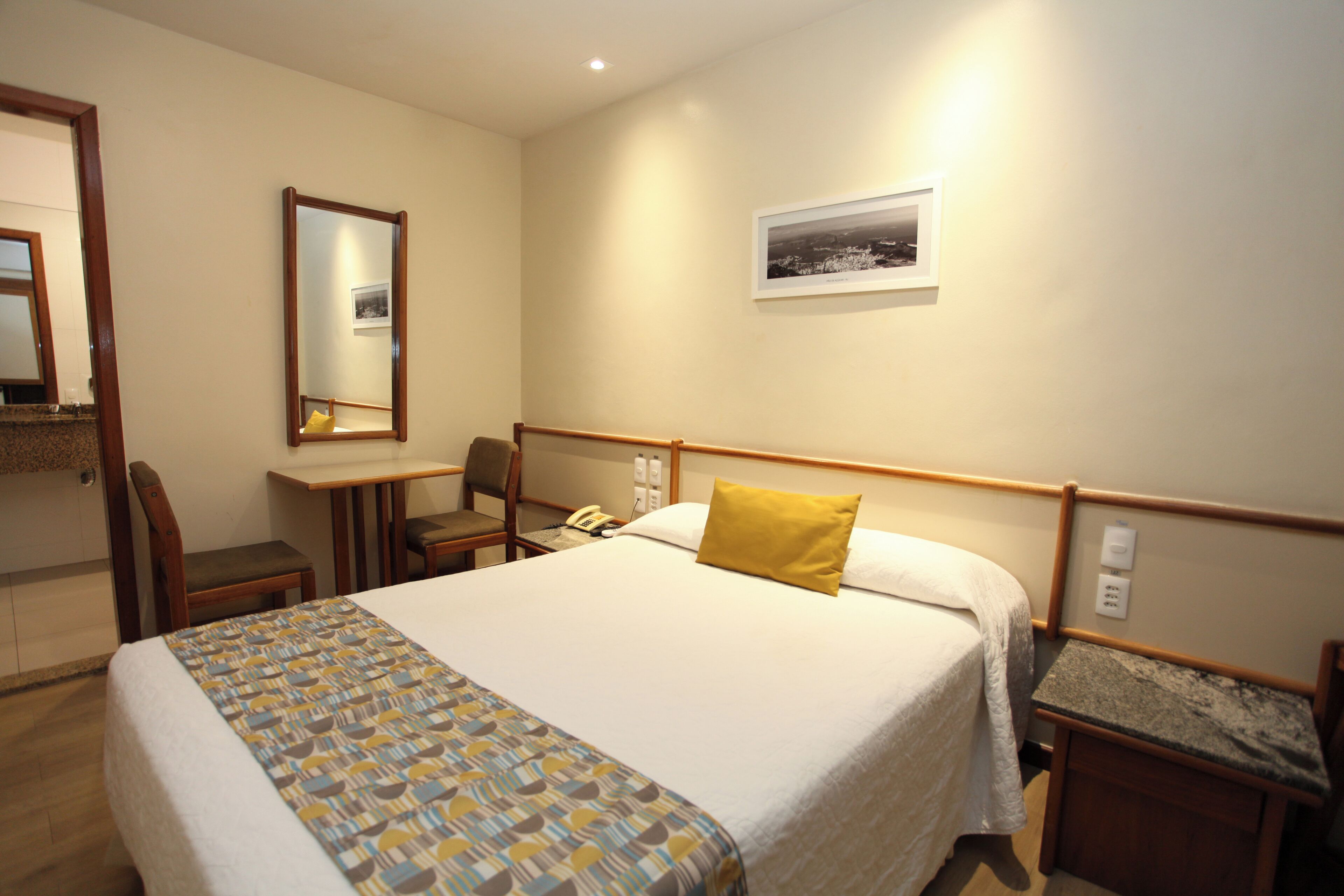 A hotel room with a bed, a desk, a chair, a telephone, and a picture on the wall.