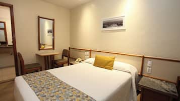 A hotel room with a bed, a desk, a chair, a telephone, and a picture on the wall.
