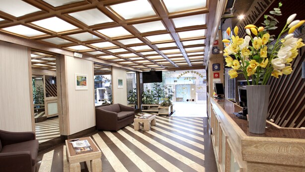 Un vestíbulo de hotel con piso a rayas, un sofá, una mesa de centro y un mostrador de recepción con un jarrón de flores.