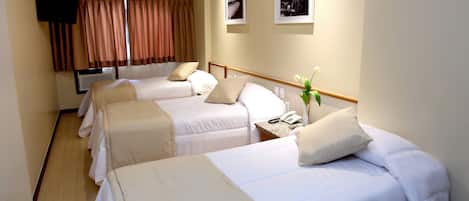 A hotel room with three single beds, a television mounted on the wall, and a window with curtains.