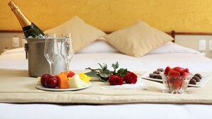 Una cama con una botella de champán, copas y una bandeja de frutas.