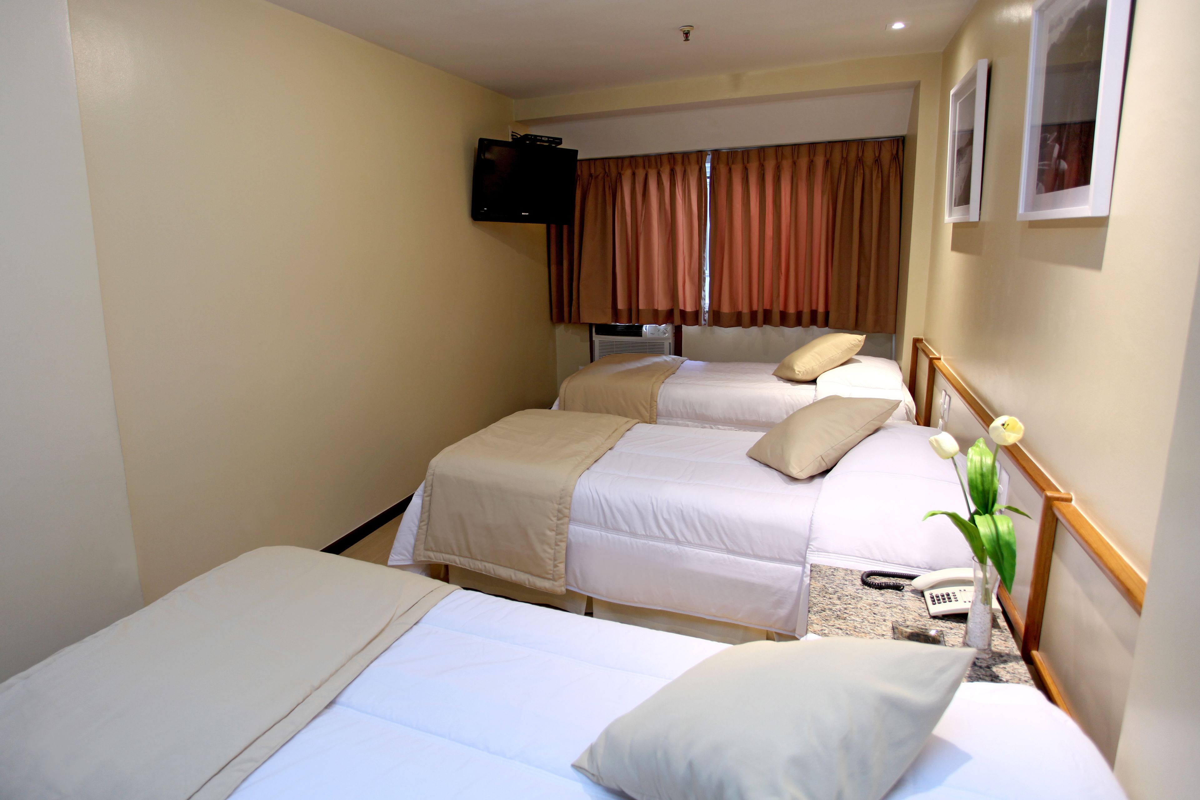 Ein Hotelzimmer mit zwei Betten, einem an der Wand befestigten Fernseher und einem Fenster mit Vorhängen.