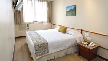 Habitación de hotel con cama, mesita de noche con teléfono, un cuadro en la pared y ventana con cortinas.