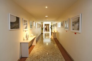 A hallway with framed pictures on the walls, a polished floor, and a central light fixture. - Mengo Palace Hotel (Rio de Janeiro)