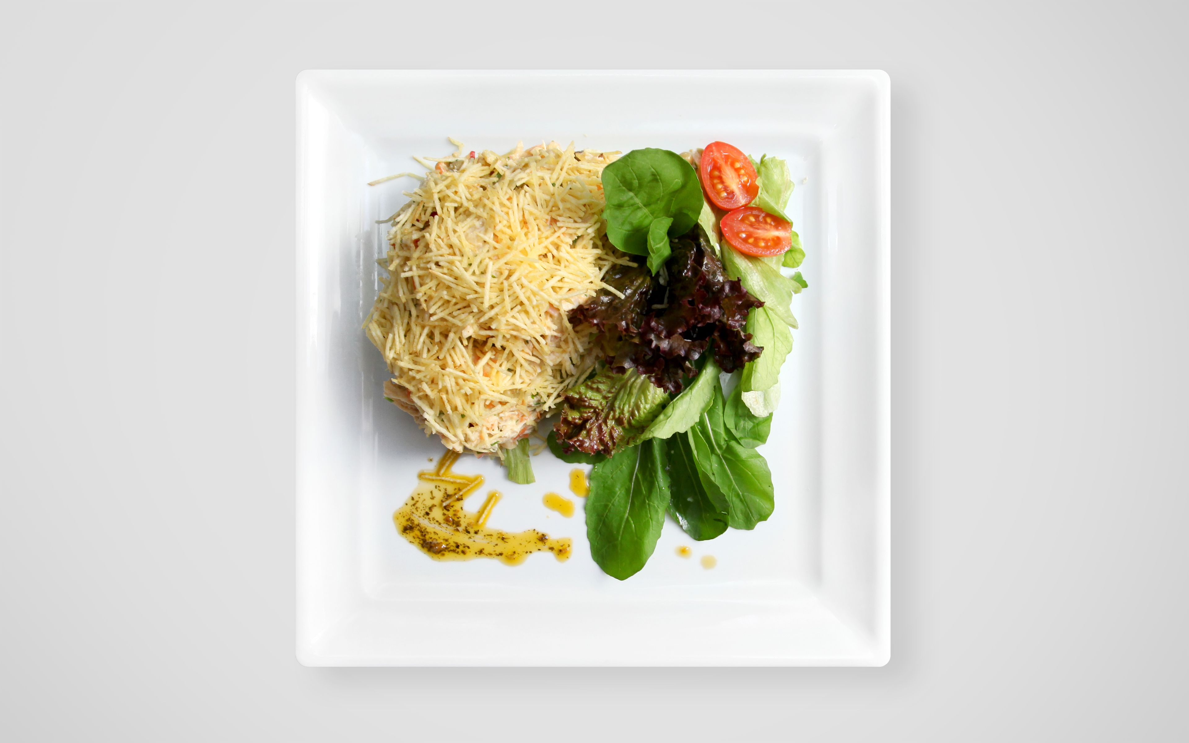 A square white plate with shredded cheese, mixed greens, and cherry tomatoes.