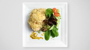 A square white plate with shredded cheese, mixed greens, and cherry tomatoes.