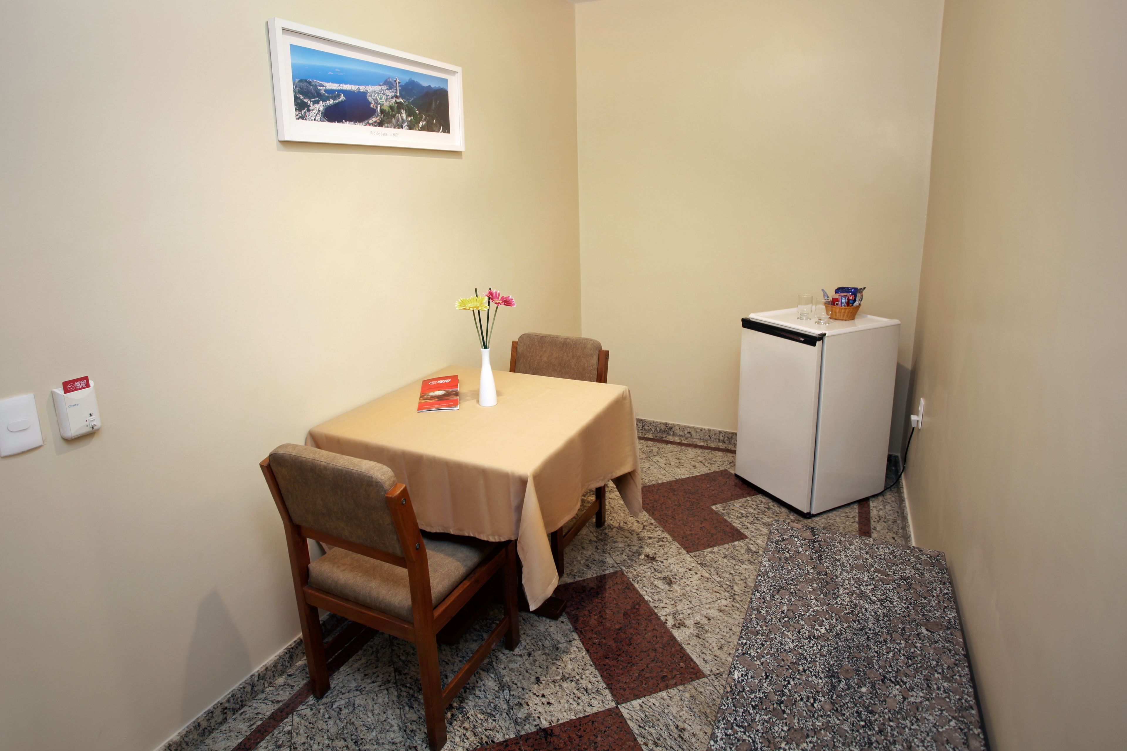 Ein kleiner Essbereich mit Tisch, Stühlen, einem Kühlschrank und einem gerahmten Bild an der Wand.