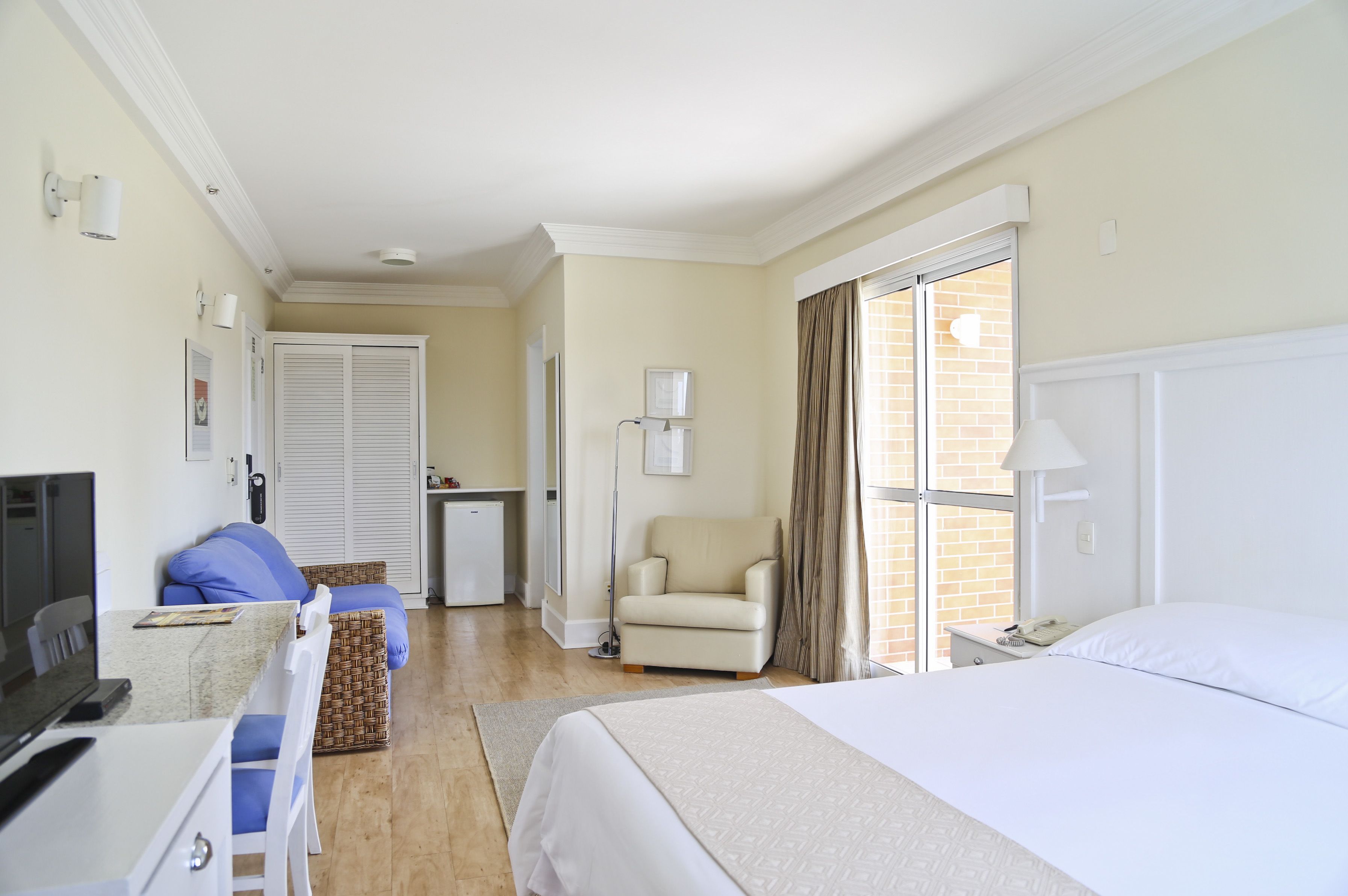 A hotel room with a bed, a desk with a computer, a chair, and a small table.