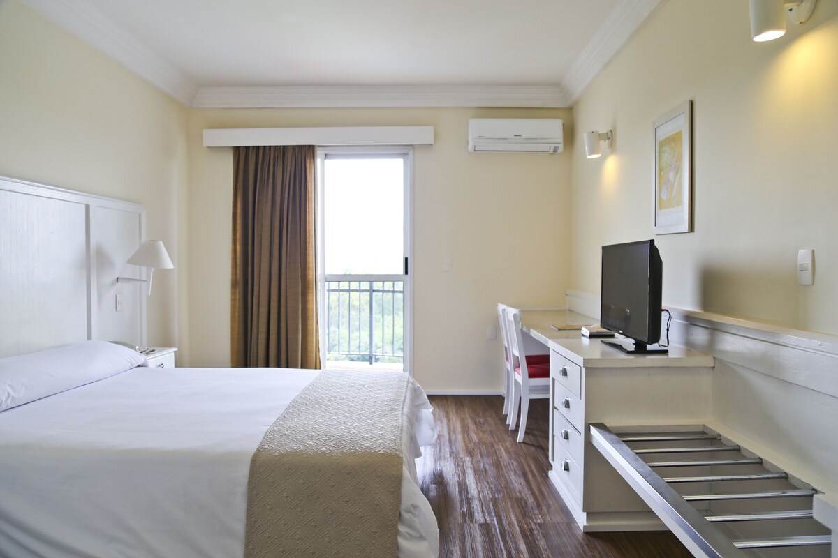 Een hotelkamer met een bed, bureau, stoel, televisie en een raam met gordijnen.