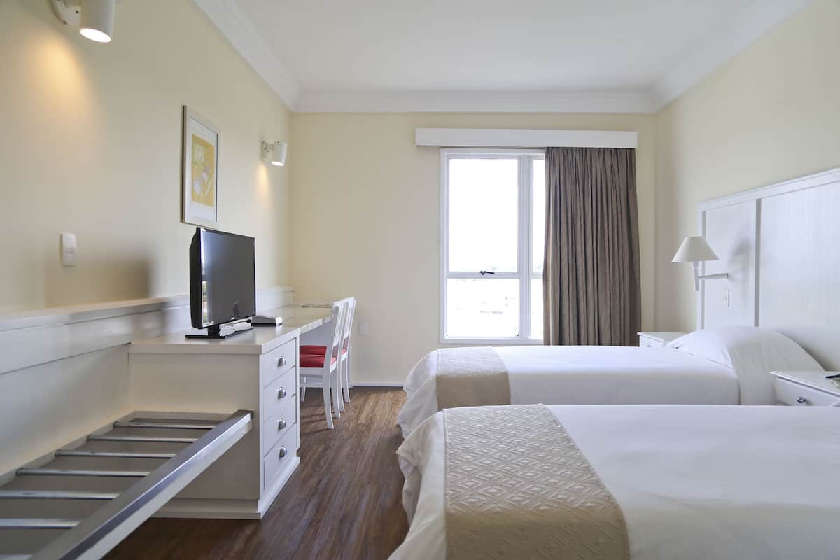 Een hotelkamer met twee bedden, een bureau met een televisie en een raam met gordijnen.