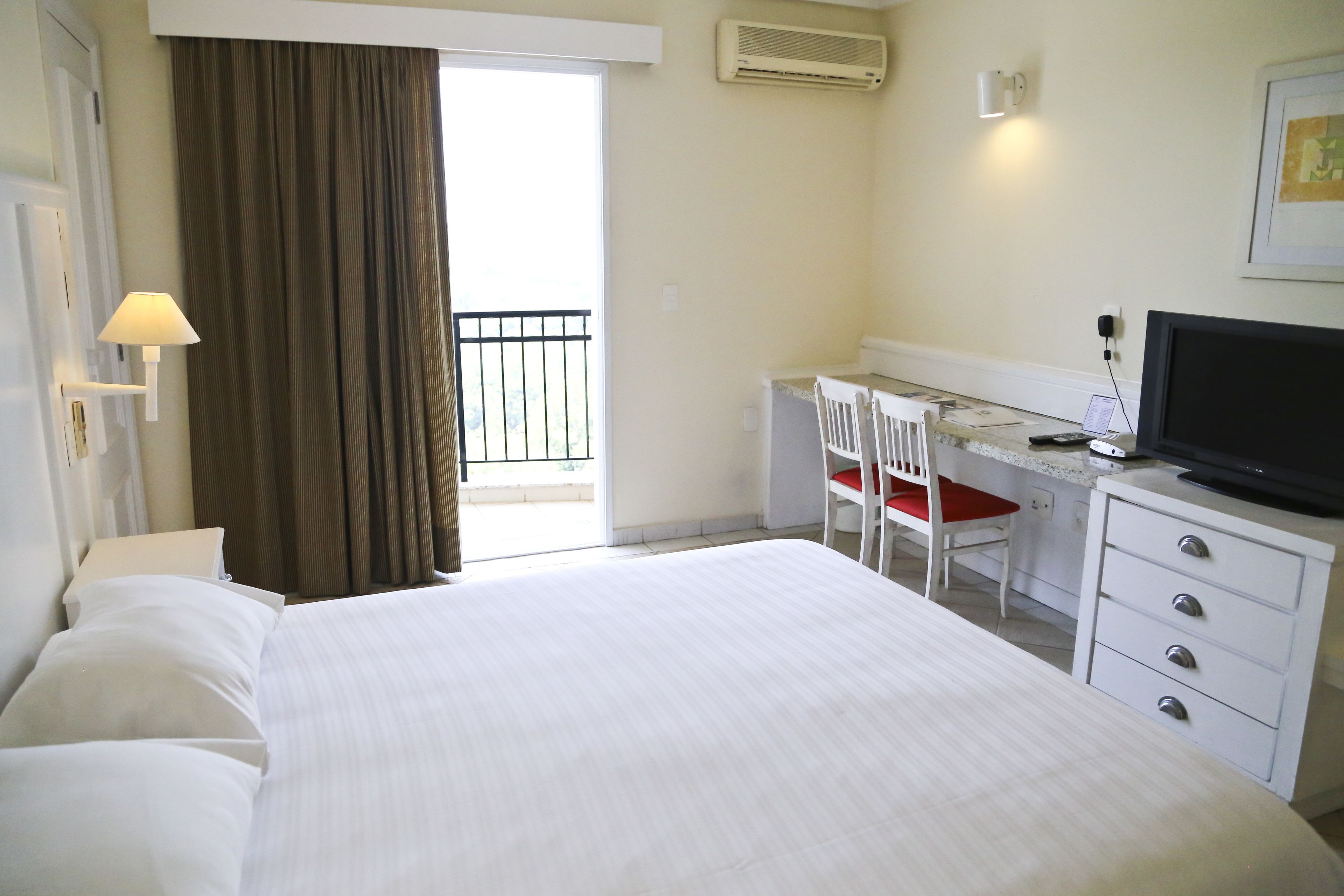 Habitación de hotel con cama, escritorio con silla, televisor y ventana con cortinas.