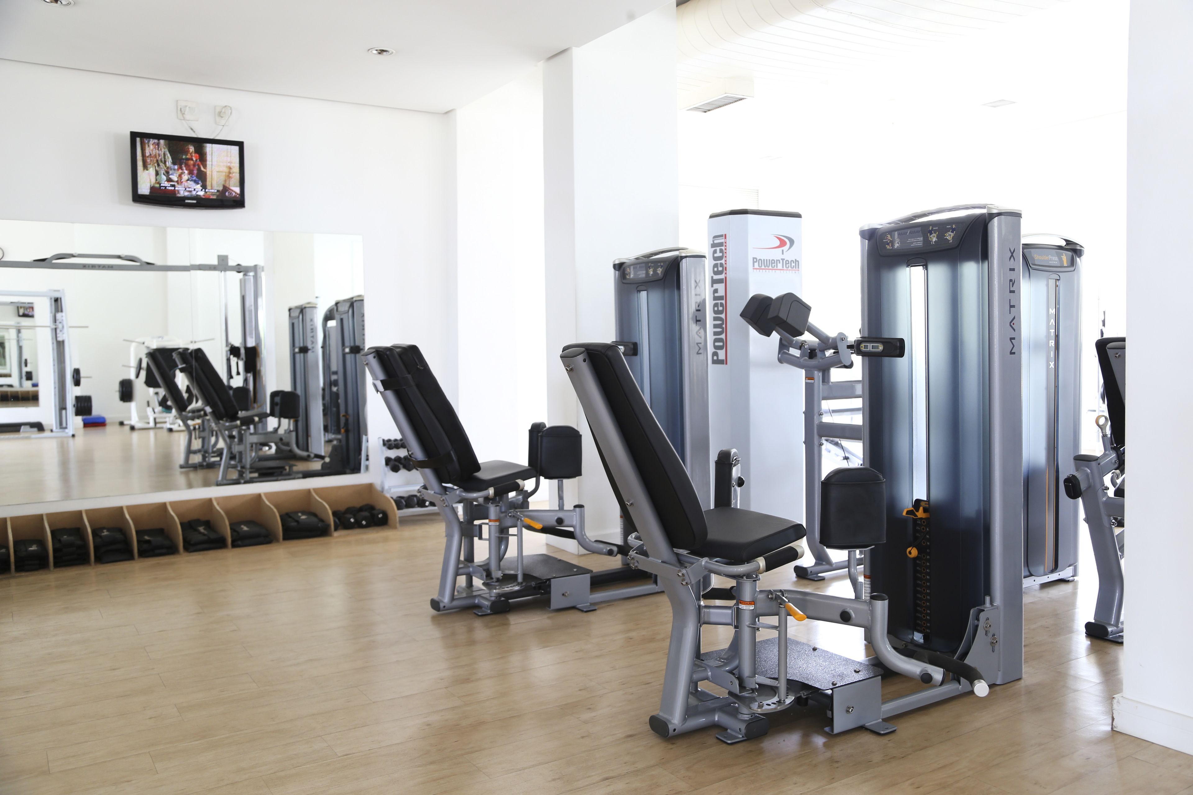 Un gimnasio con máquinas de ejercicio, un espejo grande y un televisor en la pared.