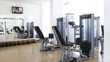 Un gimnasio con máquinas de ejercicio, un espejo grande y un televisor en la pared.