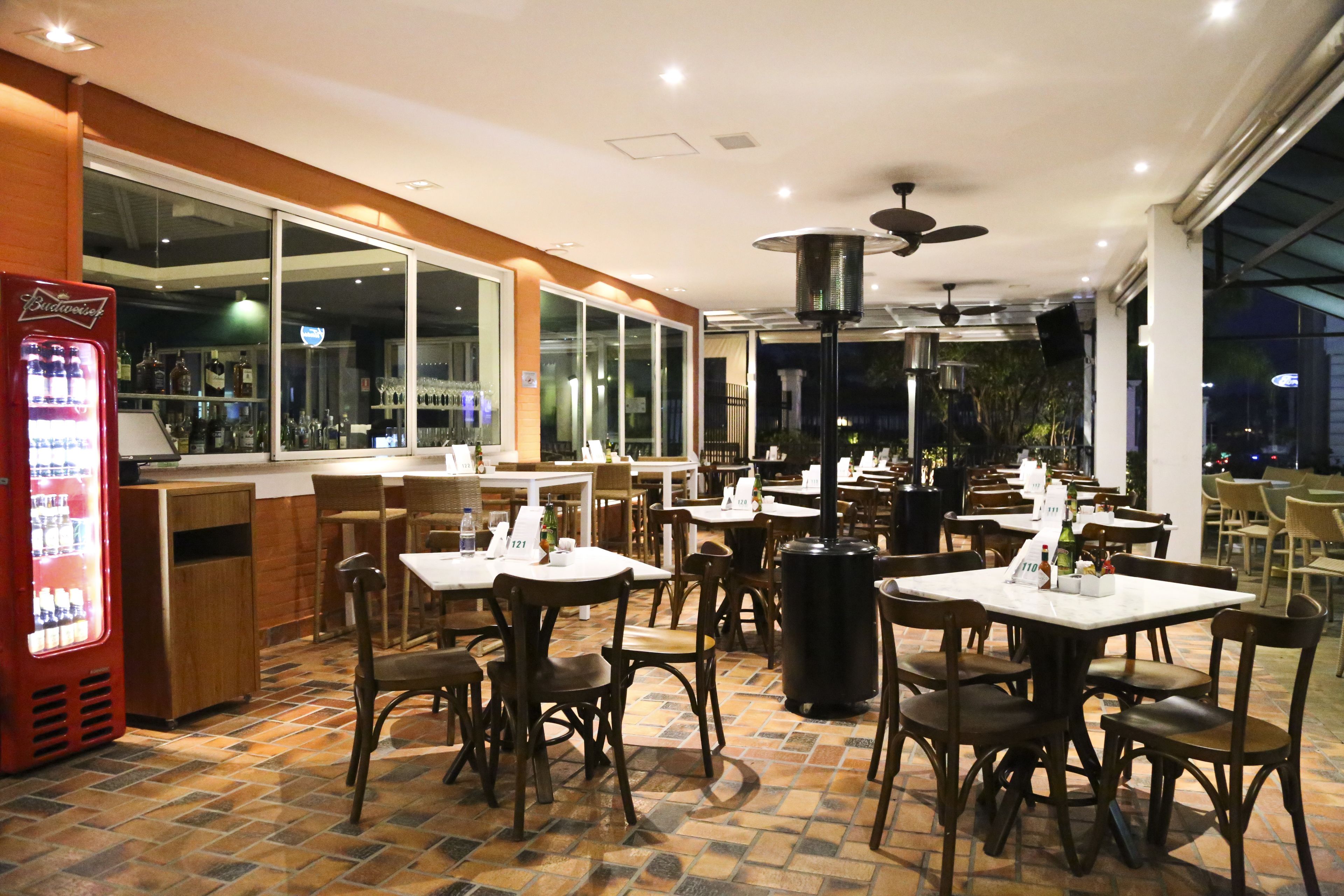 An indoor dining area with tables and chairs, a bar area with a refrigerator, and large windows.