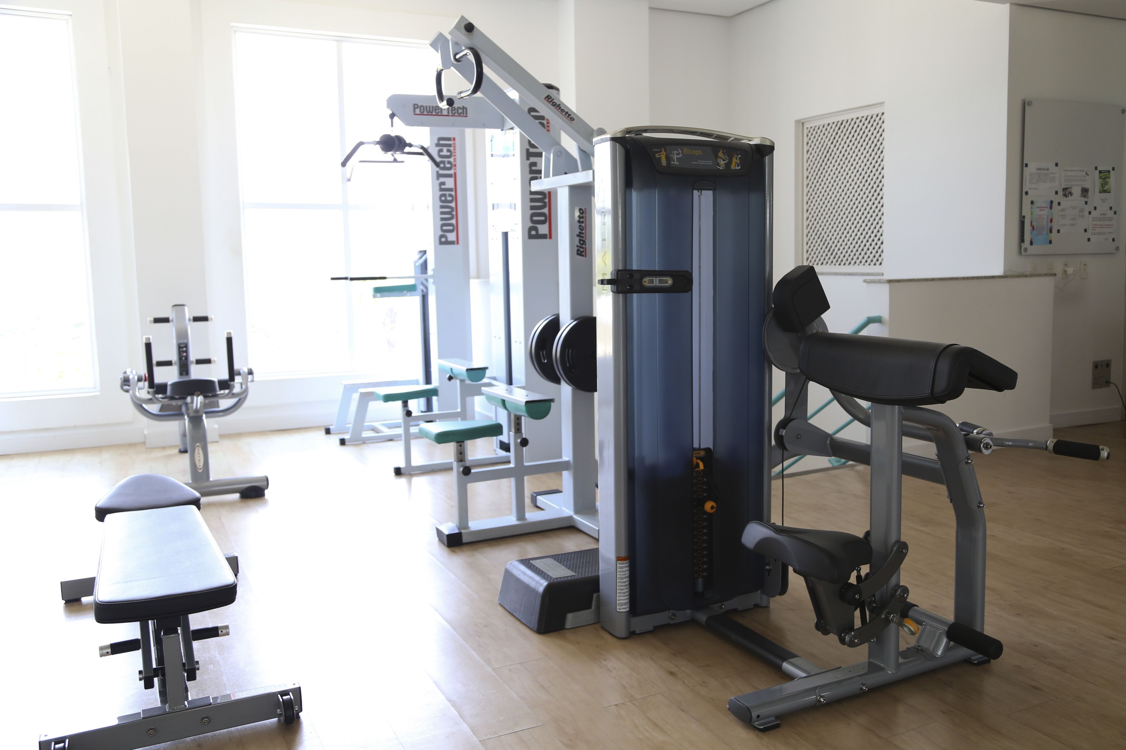 A gym with various exercise equipment, including a bench, a squat rack, and a cable machine.
