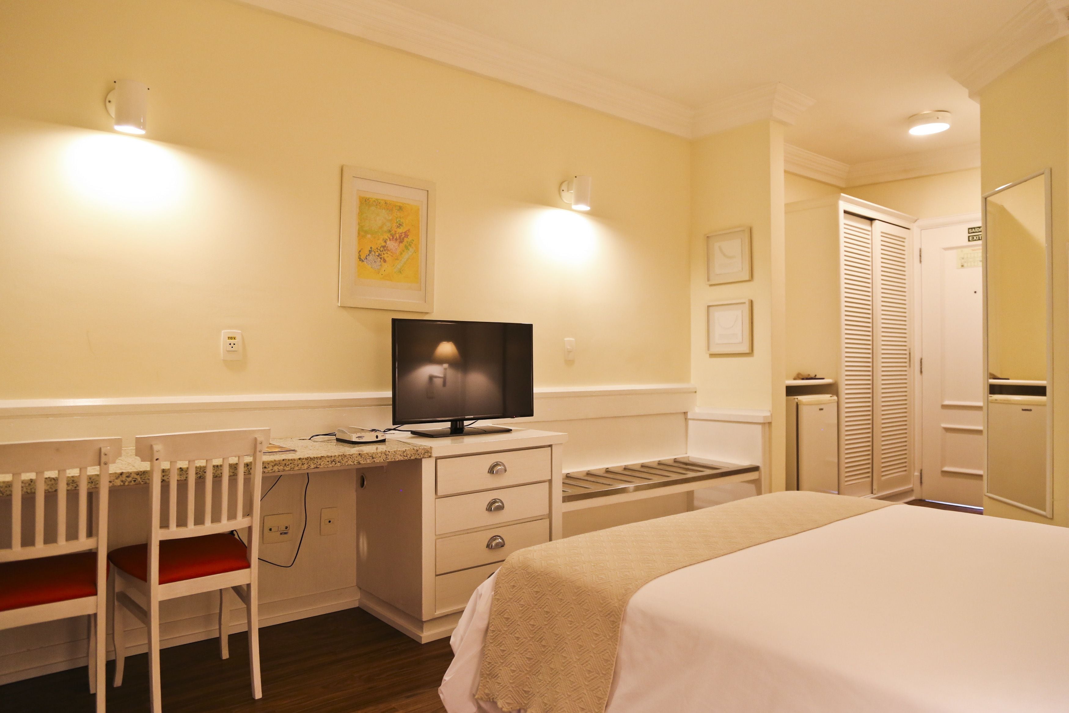 A hotel room with a bed, a desk with a television, a chair, and a wardrobe.