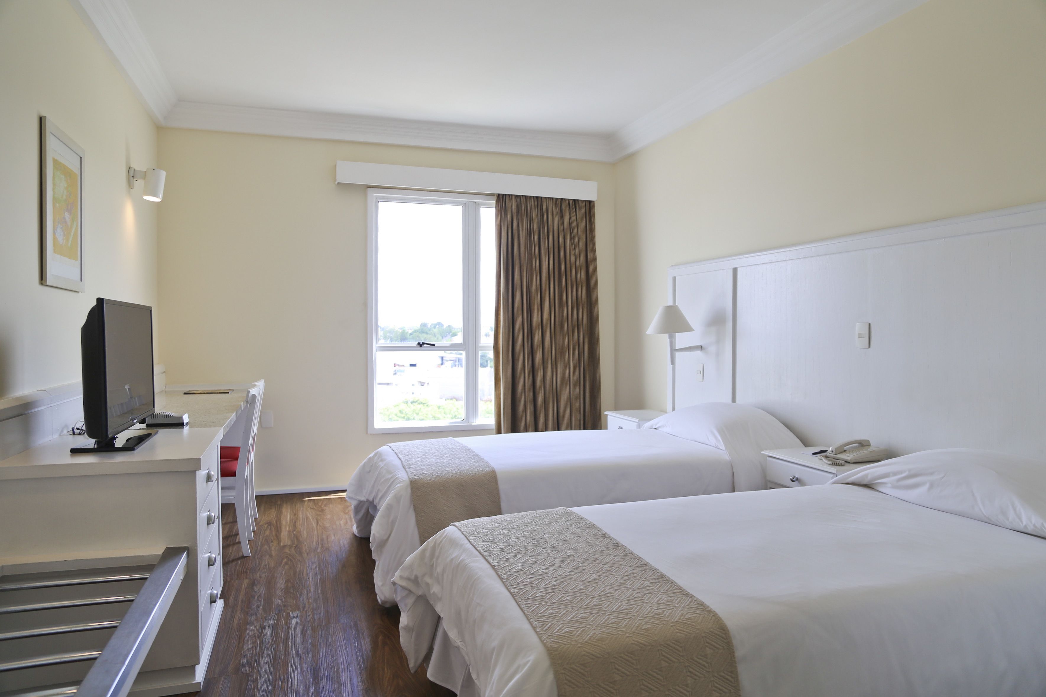 Habitación de hotel con dos camas, un escritorio con televisión y una ventana con cortinas.