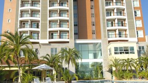 A modern hotel with a swimming pool, palm trees, and sun loungers.