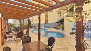 Un espacio al aire libre techado con piscina, asientos y vista a un edificio al fondo.