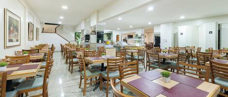 Un comedor amplio con varias mesas y sillas de madera, una cocina al fondo y obras de arte enmarcadas en las paredes.