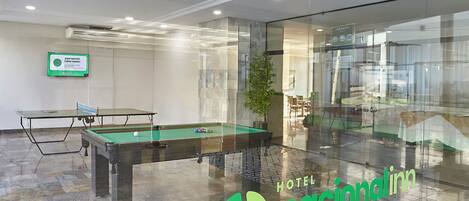 A billiards table in a hotel lobby with a glass wall and a sign for the hotel.