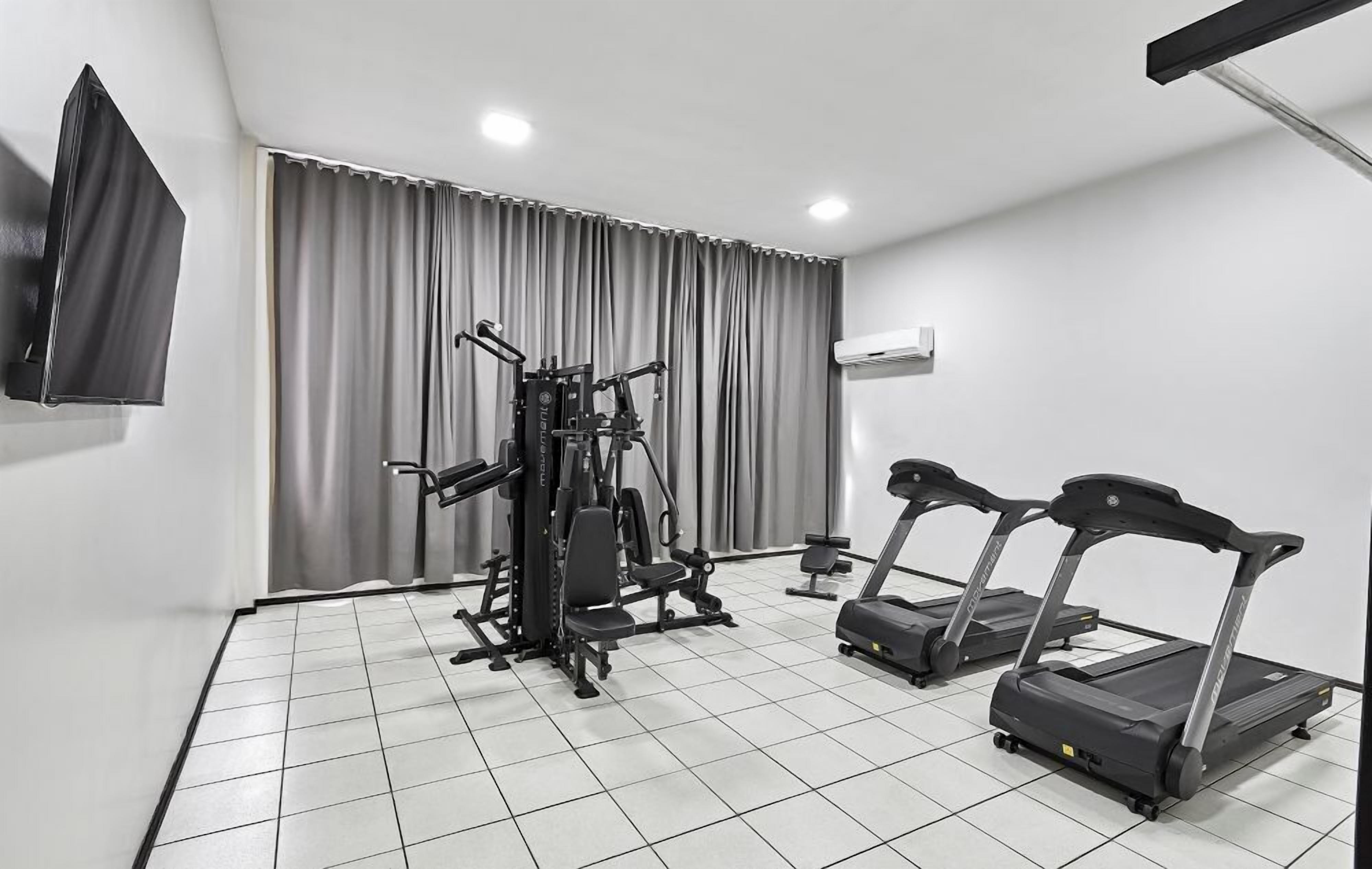 A gym with a treadmill, weight bench, and a wall-mounted TV.