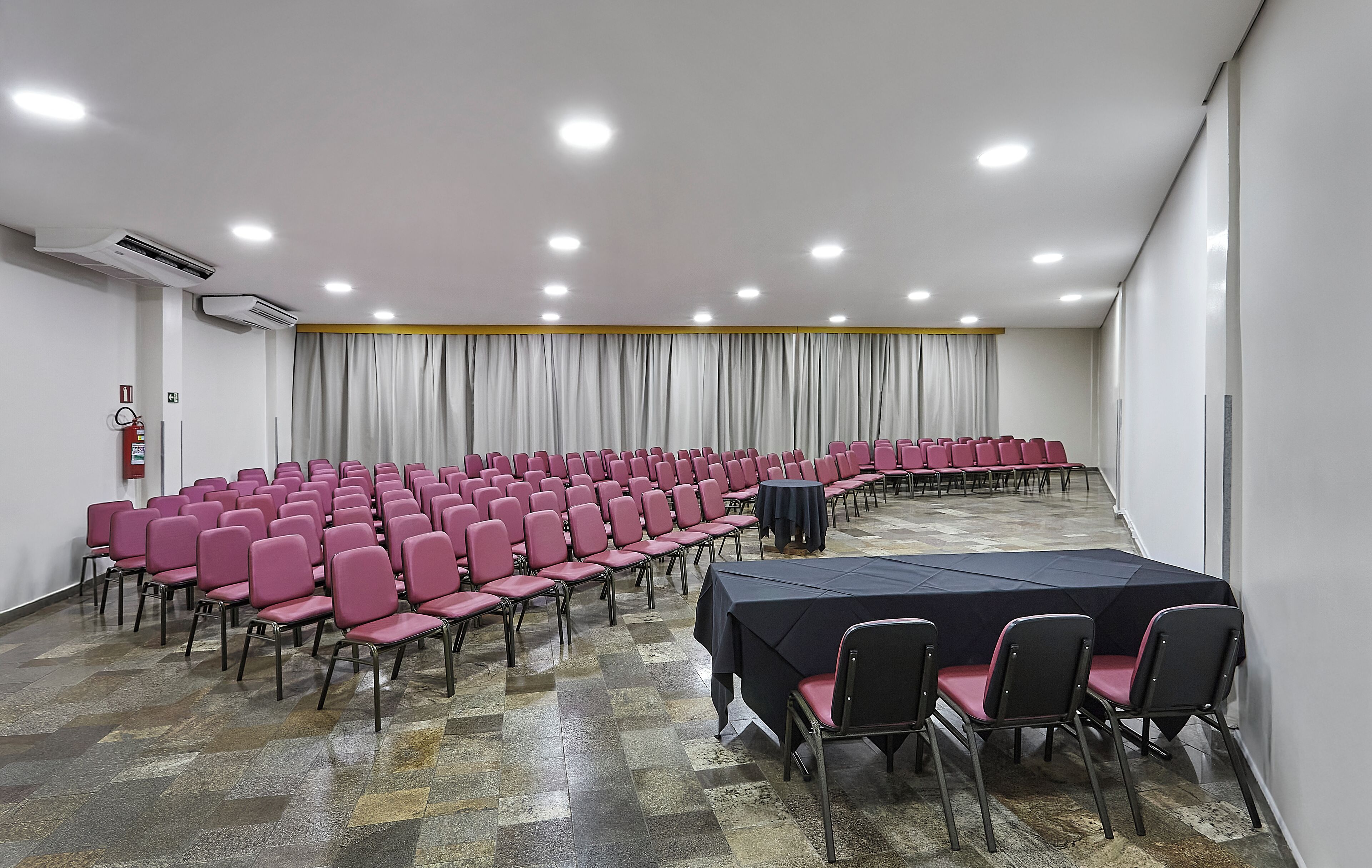 Ein Konferenzraum mit Reihen von Stühlen, einem langen Tisch und einem Feuerlöscher.
