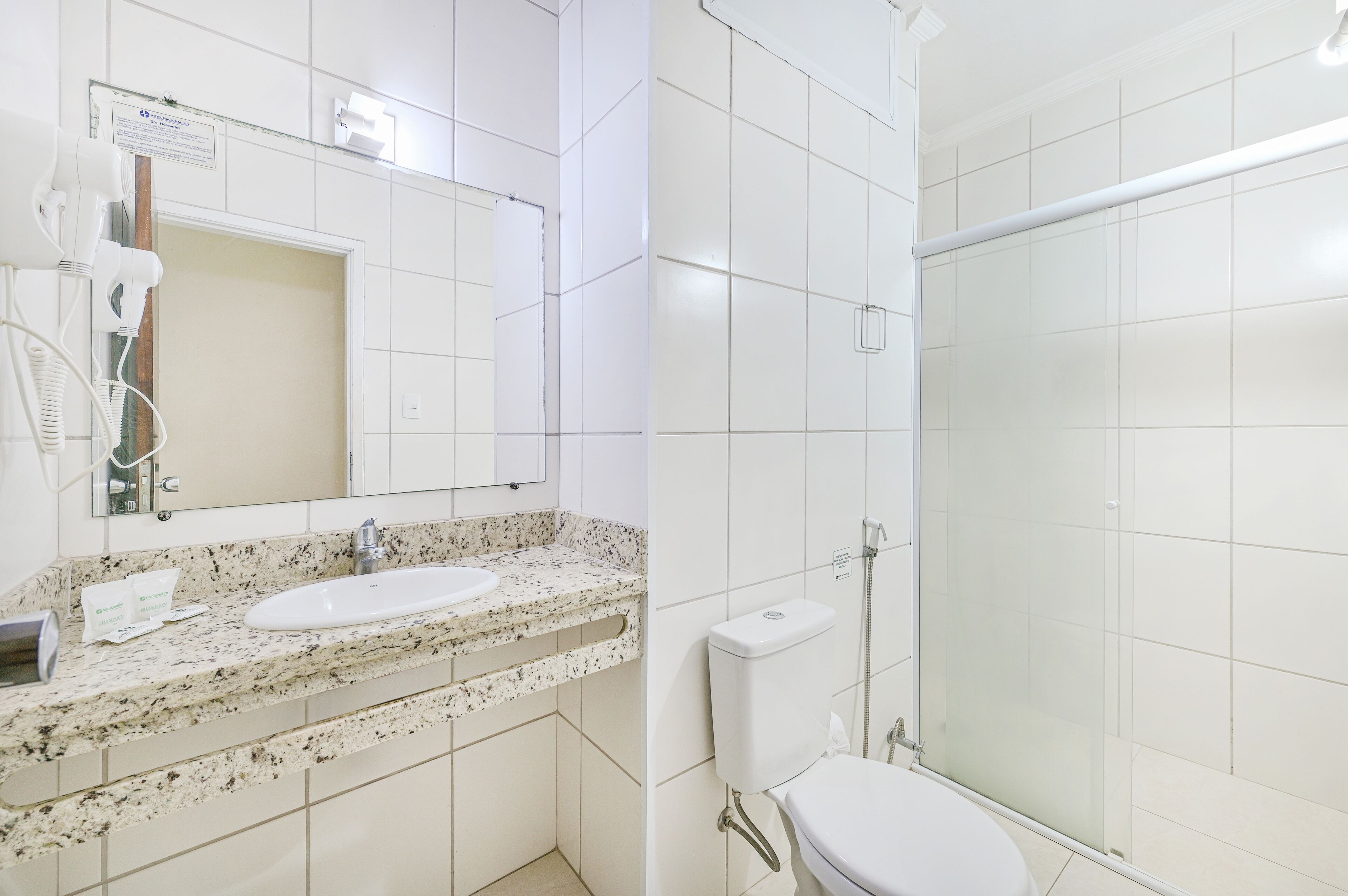 Un baño con lavamanos, espejo, secador de pelo e inodoro.