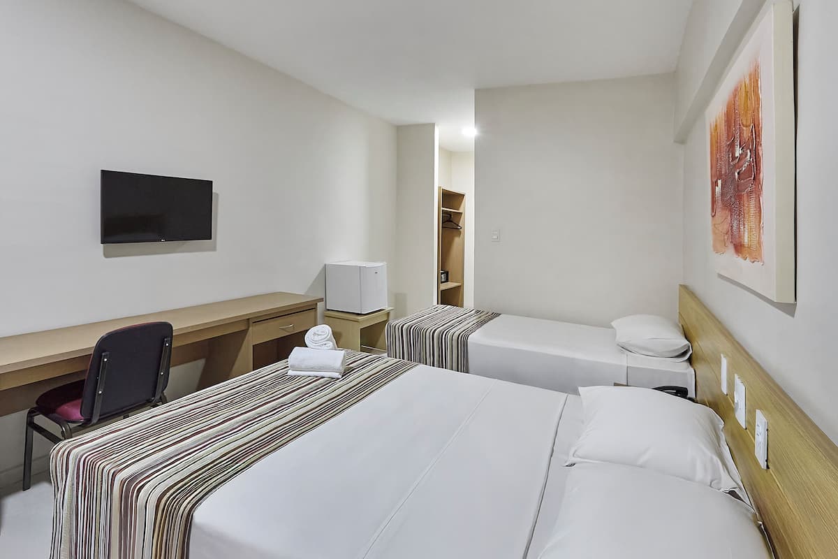 A hotel room with two beds, a desk, a chair, a TV, and a painting on the wall.