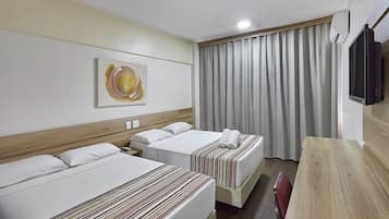 Ett hotellrum med två sängar, en sänggavel i trä, en platt-TV, en tavla på väggen och ett stort fönster med gardiner.