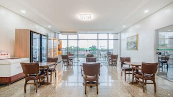 Uma ampla sala de jantar com pé direito alto e janelas grandes, com design moderno, móveis de madeira e um balcão central.