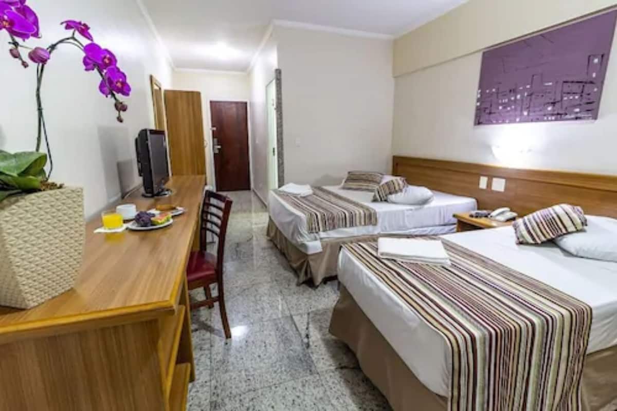 A hotel room with two beds, a desk with a chair, a television, and a wall-mounted painting.