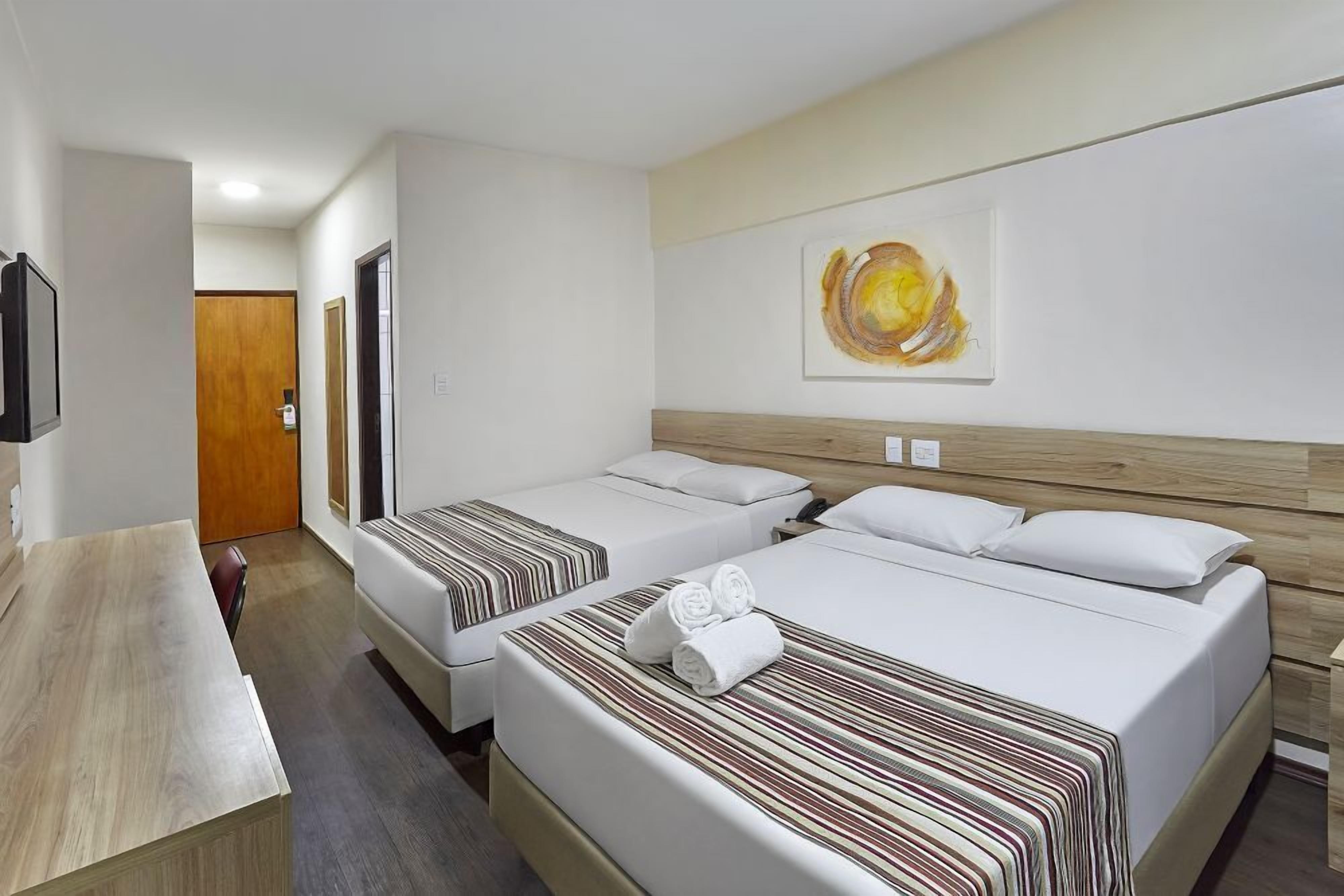 Habitación de hotel con dos camas, cabecera de madera, un cuadro en la pared y un escritorio.