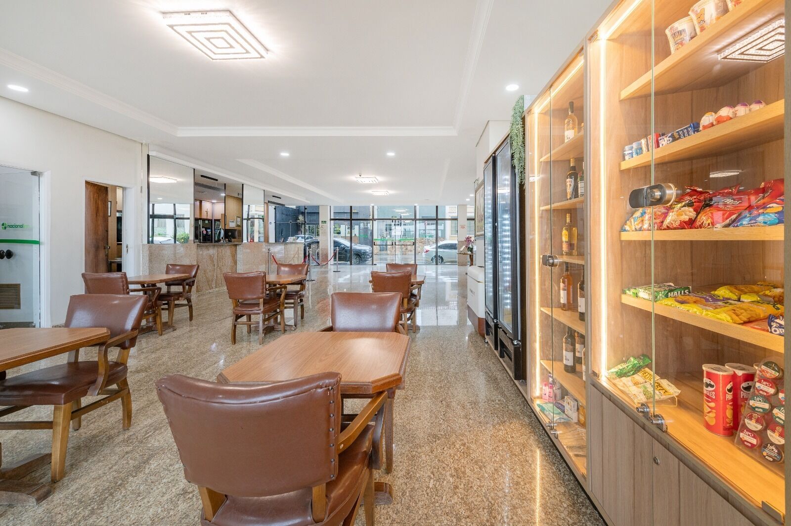 A spacious restaurant with wooden tables and chairs, a glass display case with snacks, and a view of the street through large windows.