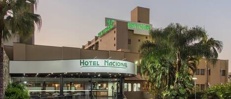 A hotel entrance with a sign reading "Hotel Nacional," surrounded by palm trees and a well-lit lobby area.
