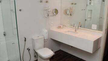 Un baño moderno con cabina de ducha de vidrio, inodoro blanco, tocador con espejo y lavamanos.