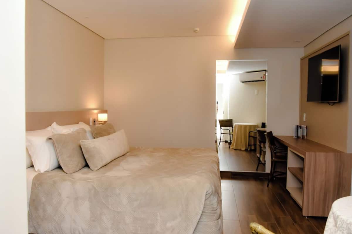 A hotel room with a bed, bedside table, and a desk with a chair.