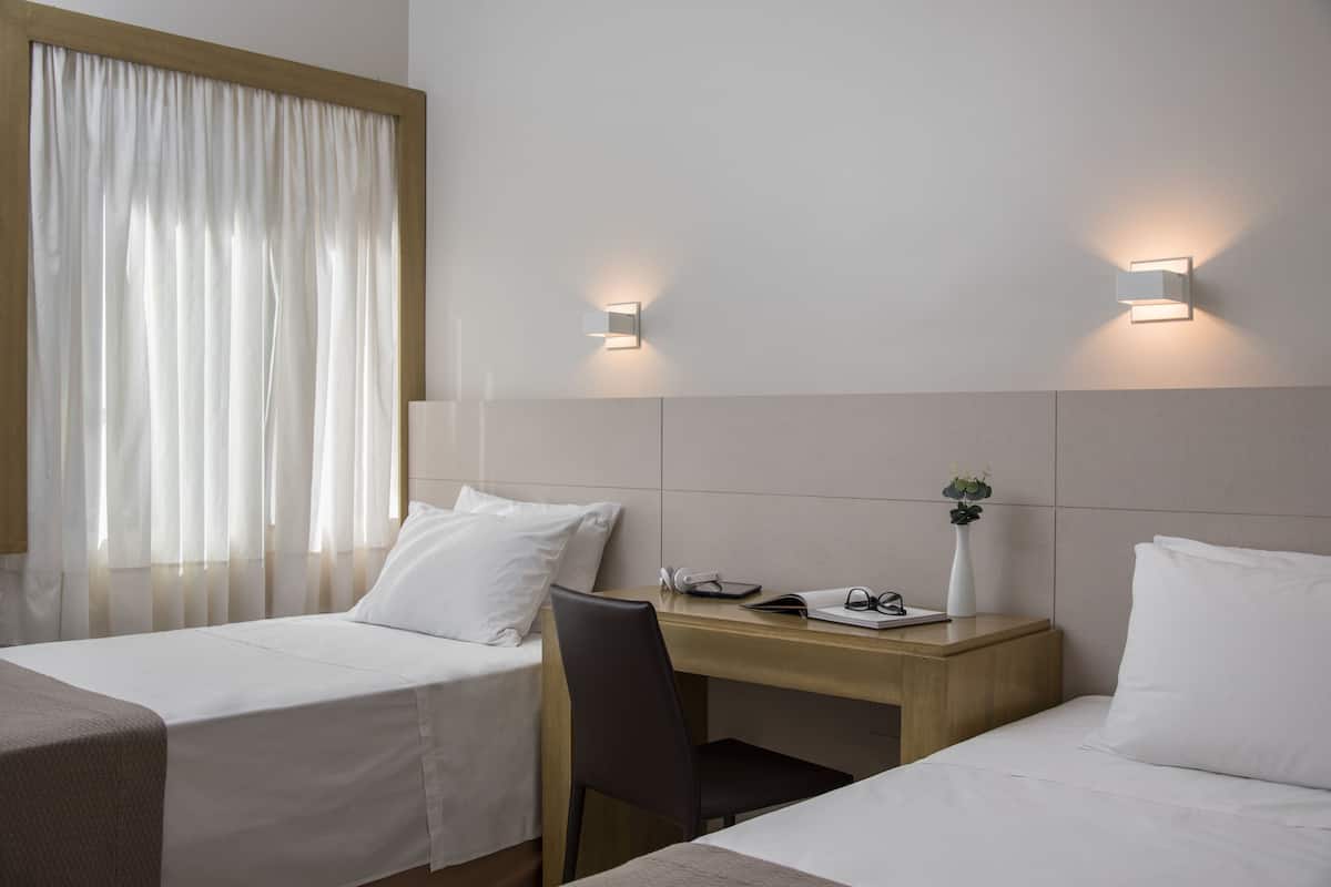 A hotel room with two beds, a desk, a chair, and two wall-mounted lights.