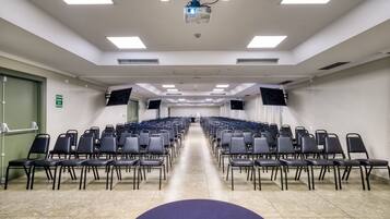 Un salón de conferencias con filas de sillas, un proyector y una pantalla grande.